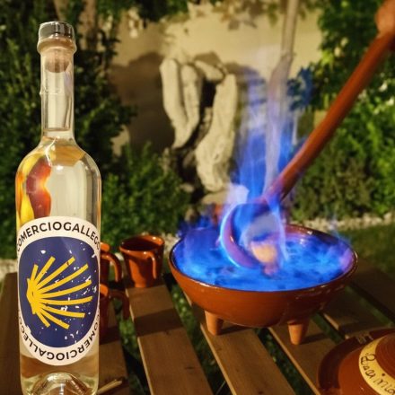 Botella de orujo gallego en una mesa con una queimada detrás ardiendo