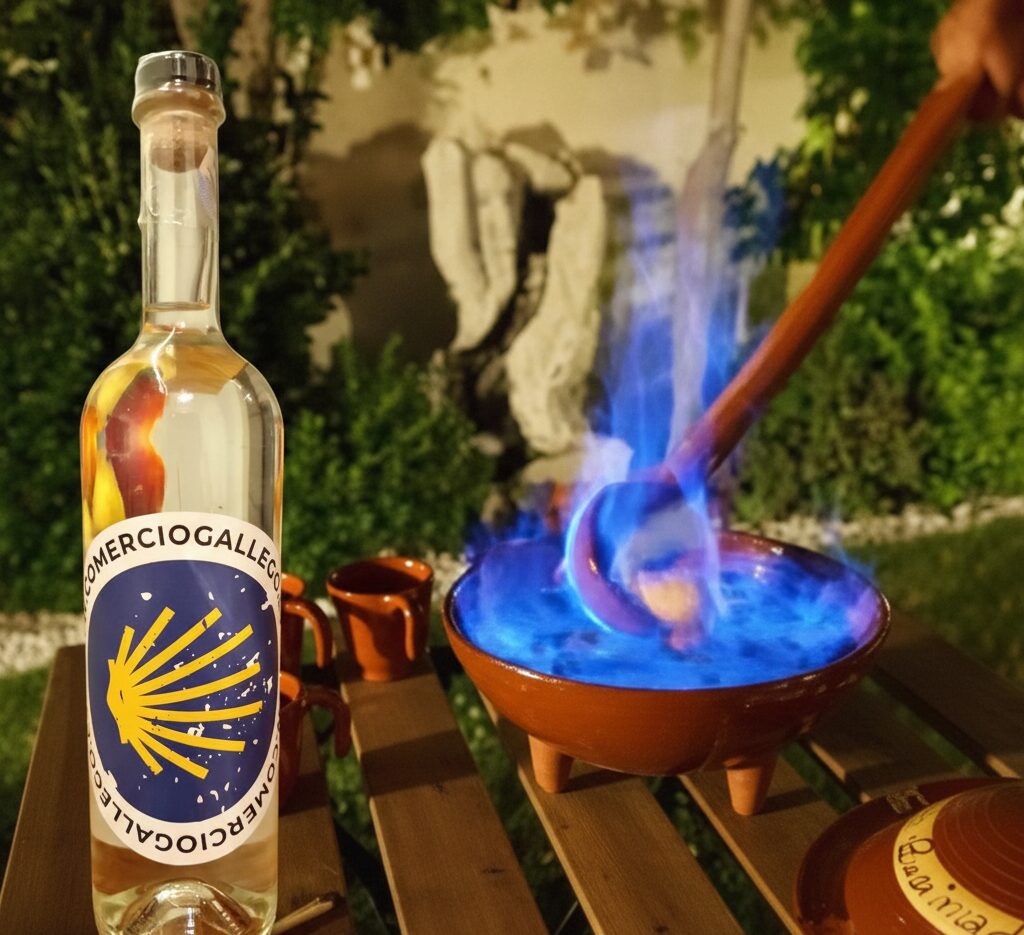Botella de orujo gallego en una mesa con una queimada detrás ardiendo