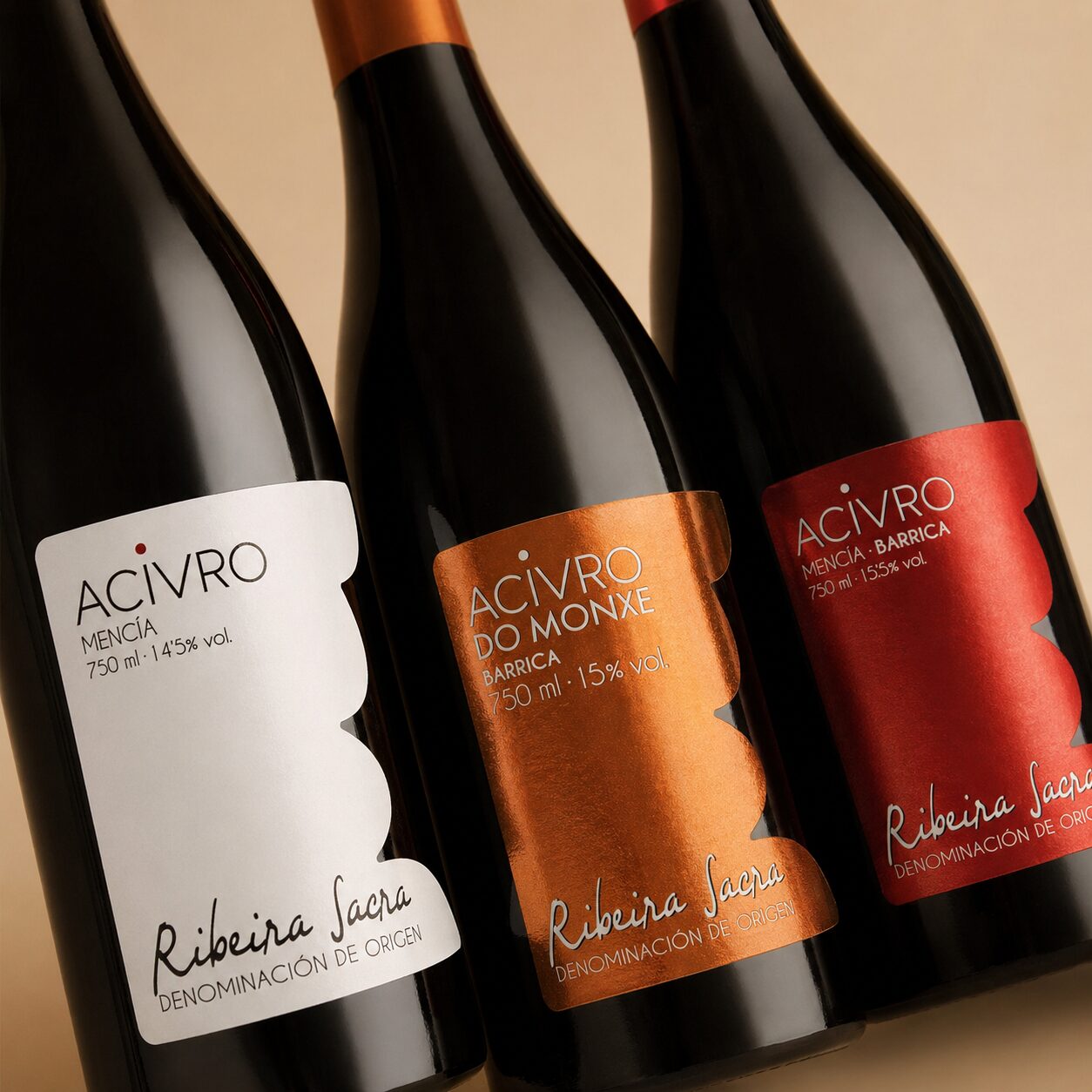 Un plano detalle en ángulo de tres botellas de vino Acivro, mostrando de cerca las texturas y acabados metalizados de las etiquetas blanca, naranja y roja de la D.O. Ribeira Sacra.
